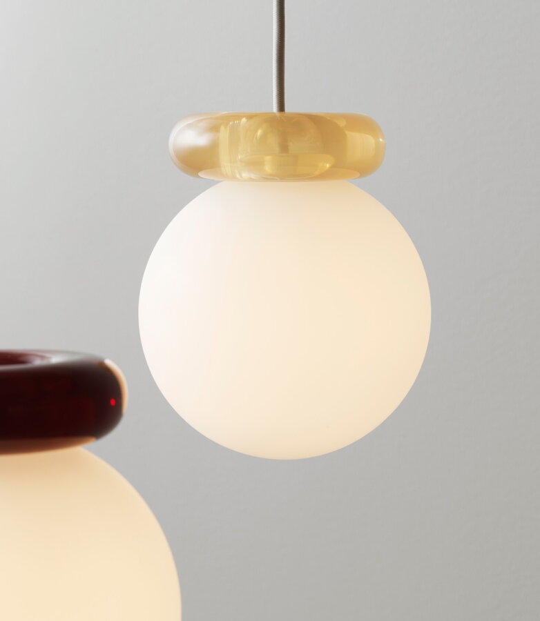 Biela okrúhla lampa zo skla a s dizajnovým živicovým prstencom v pieskovej farbe.