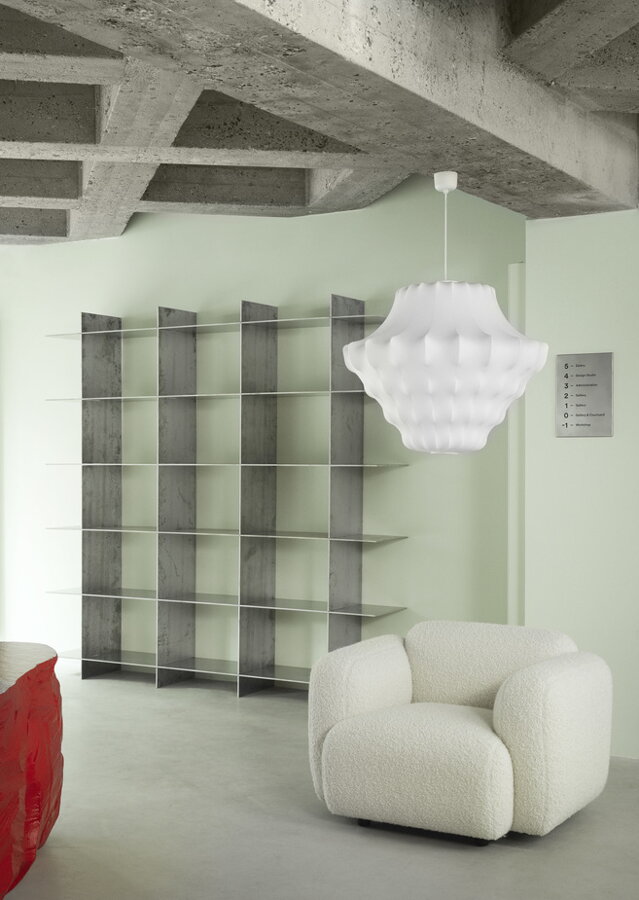 Biela závesná lampa visiaca z betónového stropu na bielym čalúneným kreslom.