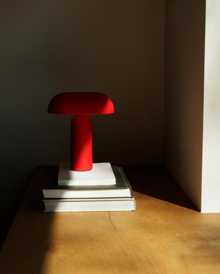 Červená stolová lampa položená na kôpke knižiek položených na drevenej podlahe