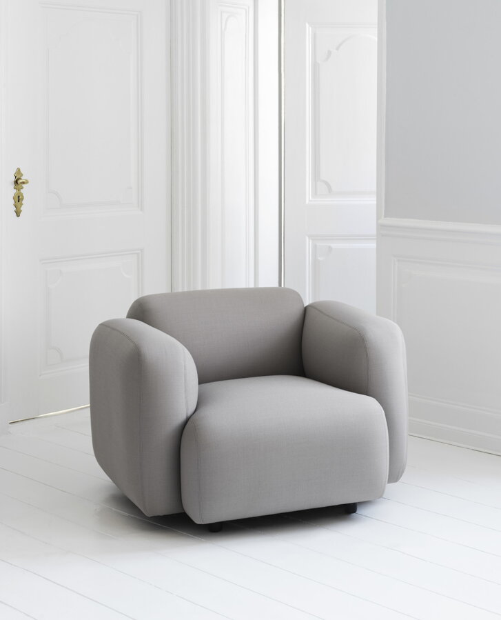 Sivé kreslo Swell Armchair vo svetlej bielej miestnosti s bielymi stenami.