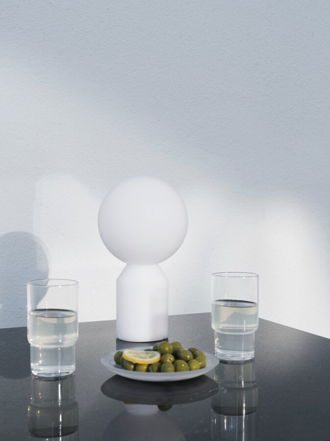 Dizajnová stojaca lampa položená pri pohárikoch na príručnom stolíku. 