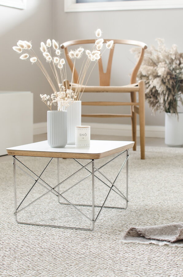 Plastový koberec MONO Linen/Vanilla ľanovej farby s béžovým príručným stolíkom s bielou vázou a kvetmi.